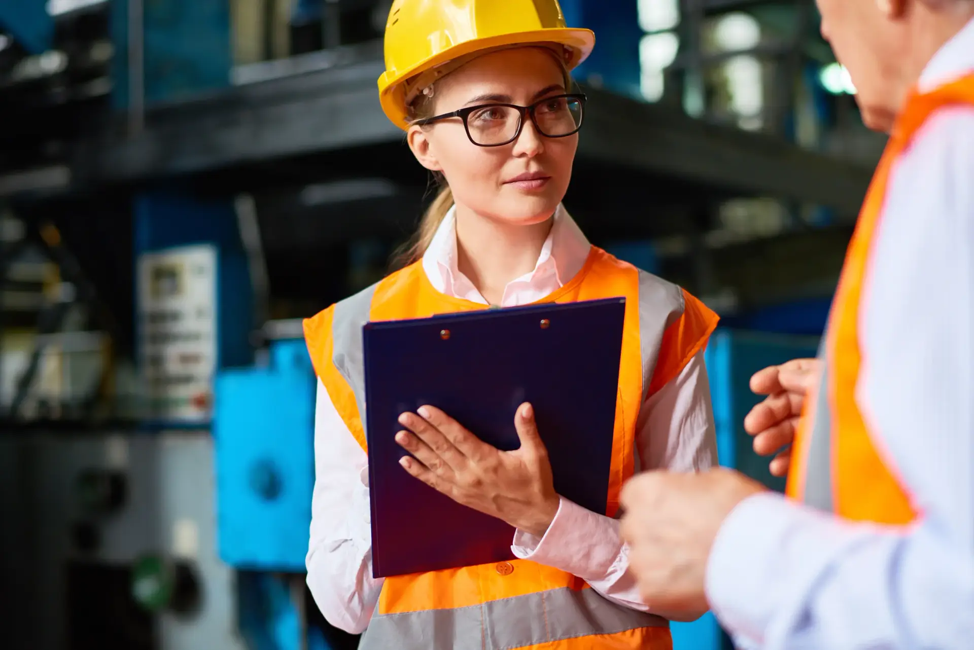 Fachkraft für Arbeitssicherheit mit Klemmbrett bei einer Begehung in der Werkshalle